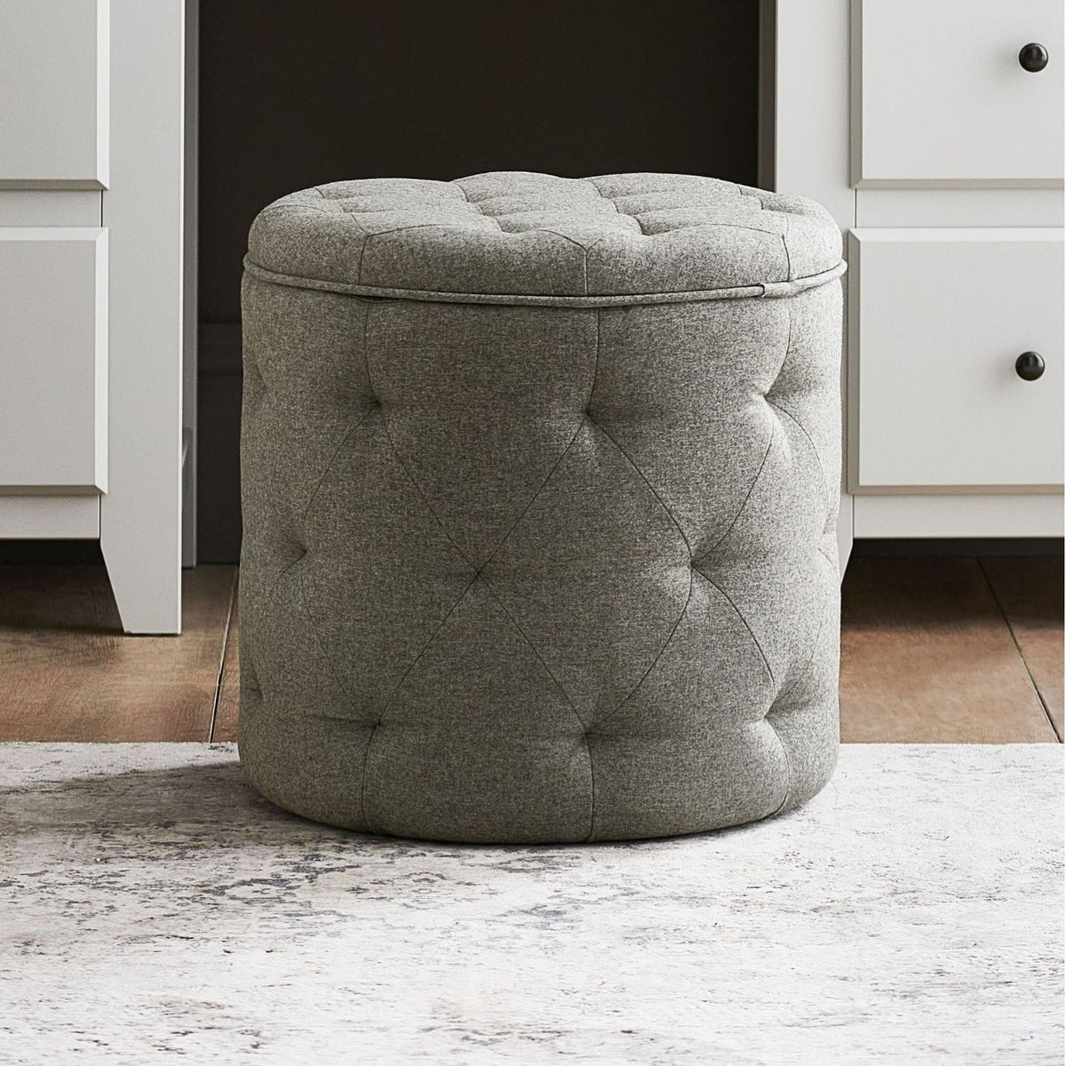 Gray tufted ottoman in a room with white cabinets.