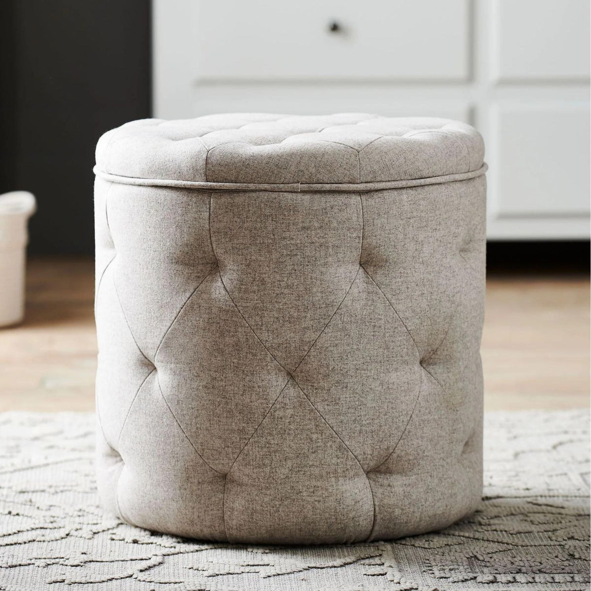 Beige tufted storage ottoman on a textured rug with a blurred background