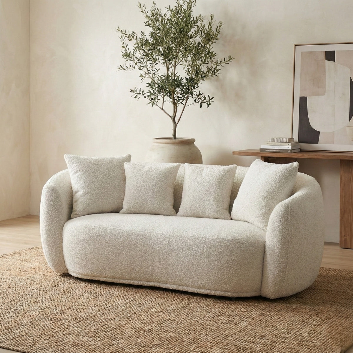 Beige sofa with white cushions in a living room setting with a plant and abstract art.