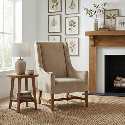 Beige armchair in a living room with a side table, lamp, and fireplace.