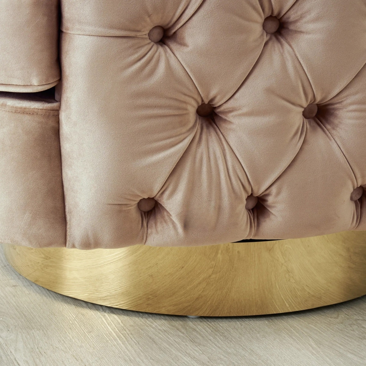 Close-up of a tufted pink velvet chair with a gold base on a light wooden floor.