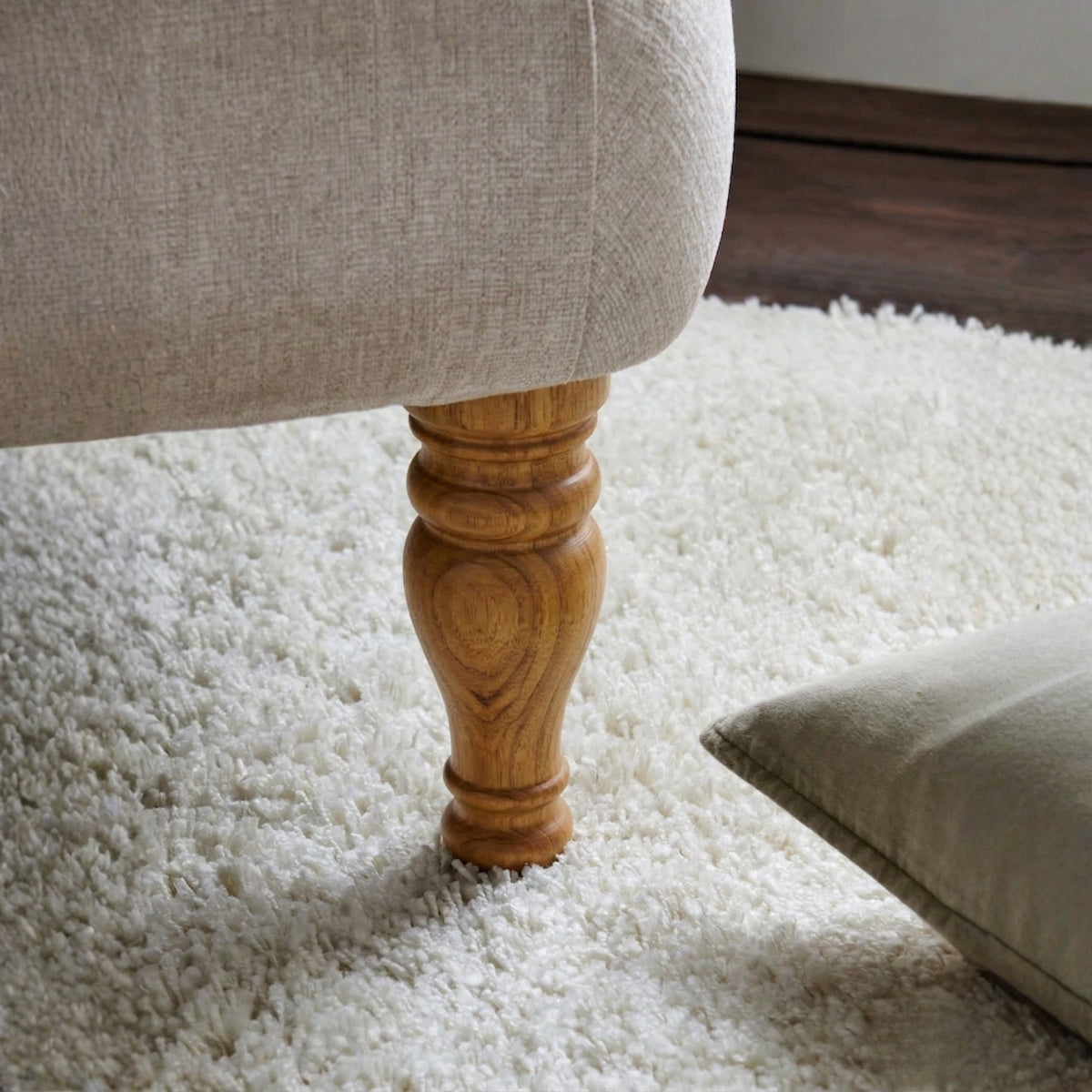 Close-up of a wooden furniture leg on a white carpet with a neutral-colored sofa in the background.